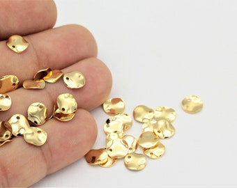 May include: A group of gold-colored metal charms in the shape of a circle with a slightly irregular edge. The charms have two small holes at the top.