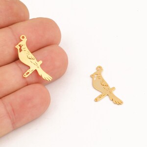 Puede incluir: Dos abalorios de metal de color dorado con forma de pájaro cardenal. Los abalorios están detallados con las plumas del pájaro y tienen un bucle en la parte superior para sujetarlos a un collar o pulsera.
