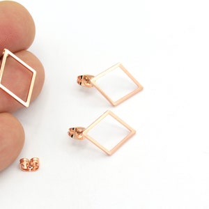 Pode incluir: Um par de brincos em forma de diamante em ouro rosa com um design simples e minimalista. Os brincos são feitos de metal e têm um acabamento polido.