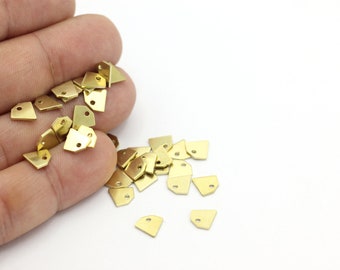 May include: A pile of small, gold-colored metal charms in the shape of a triangle with a hole at the top. The charms are scattered on a white surface.