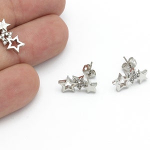 Puede incluir: Un par de pendientes de estrella plateados con pequeñas piedras transparentes en el centro de cada estrella.