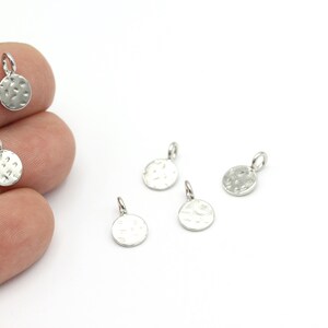 May include: Five silver-toned metal charms in the shape of a circle with a hammered texture. Each charm has a small loop at the top for attaching to jewellery.