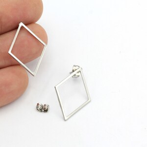 Pode incluir: Um par de brincos geométricos prateados com formato quadrado. Os brincos são feitos de metal fino e têm um design simples e moderno.