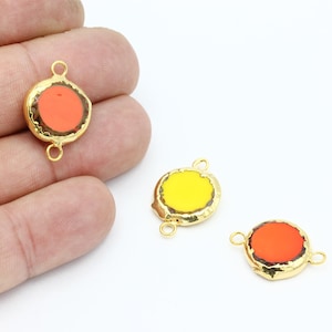 Op de afbeelding: Drie goudkleurige metalen bedels met een rond, plat, gekleurd glazen hart. De bedels hebben twee springringen om aan sieraden te bevestigen. De kleuren van de glazen harten zijn oranje, geel en rood.