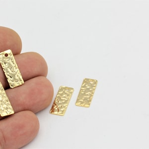 Puede incluir: Cuatro etiquetas rectangulares de metal de color dorado con textura martillada y un agujero en la parte superior.