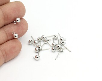 May include: A close-up of a pile of silver-toned earring findings with a round ball head and a straight pin. The findings are scattered on a white surface.