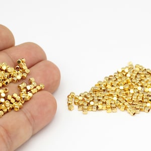 Peut inclure: Un tas de petites perles en métal de couleur dorée. Les perles sont cubiques et ont une finition brillante.