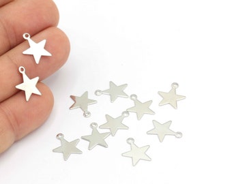Puede incluir: Una colección de dijes de estrella de metal plateado con un bucle en la parte superior. Los dijes están esparcidos sobre una superficie blanca.