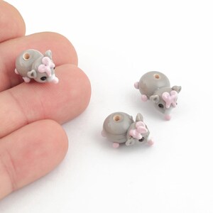 Puede incluir: Tres cuentas de vidrio gris con forma de animal pequeño con orejas rosas y nariz blanca. Las cuentas tienen un agujero en el centro para enhebrar.