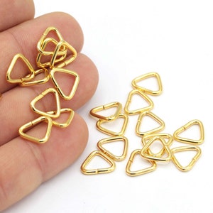 May include: A close-up of a pile of gold-colored triangle-shaped metal rings. The rings are about 1 inch in diameter and have a smooth finish.