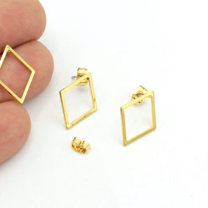 Pode incluir: Um par de brincos de forma de diamante de cor dourada com um design simples e minimalista. Os brincos são feitos de um fio metálico fino e têm um fecho de poste.