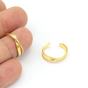 May include: Two gold-toned adjustable rings with a criss-cross design. The rings are made of metal and have a smooth finish.