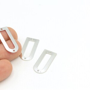 May include: Three silver metal rectangular-shaped tags with rounded corners and a hole in the center of each tag.