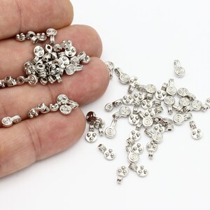 May include: A large quantity of silver-toned metal bead caps with a decorative swirl design. The caps have a small loop at the top for attaching to jewelry.