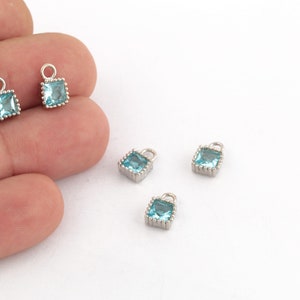 May include: Four silver charm pendants with light blue square-shaped gemstones. Each pendant has a small loop at the top for attaching to a chain or bracelet.