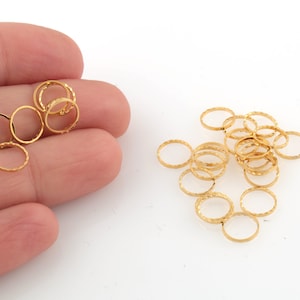 Puede incluir: Un montón de anillos de salto de color dorado, algunos están en una mano, otros están esparcidos sobre una superficie blanca.