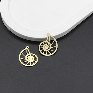 May include: Two gold-colored metal charms shaped like nautilus shells. The charms are intricately detailed and have a cutout design.