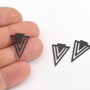 May include: Three matte black metal charms in a geometric arrowhead shape. Each charm features a central solid triangle surrounded by two nested open triangular frames, with two small circular holes at the top for attachment purposes.