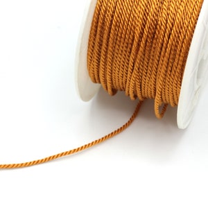 May include: A spool of gold cord, with a length of cord extending from the spool.