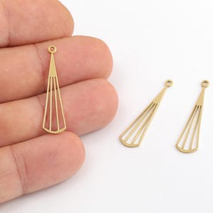 May include: Three gold-toned metal jewelry charms, each featuring a long, slender, triangular fan shape with a series of vertical cutouts and a small circular loop at the top for attachment, presented in a clean, minimalist design.