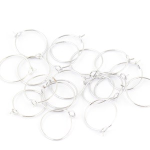May include: A group of silver hoop earrings, all of the same size and style, are piled together on a white background.