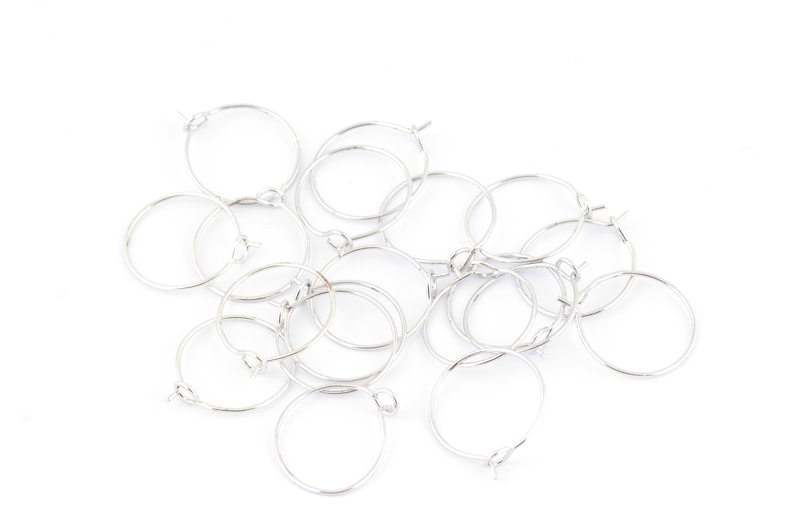 May include: A group of silver hoop earrings, all of the same size and style, are piled together on a white background.
