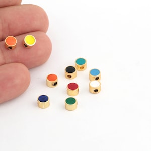 Puede incluir: Surtido de pequeñas cuentas redondas de color dorado con tapas de esmalte de diferentes colores. Los colores incluyen rojo, naranja, amarillo, verde, azul, negro y blanco.