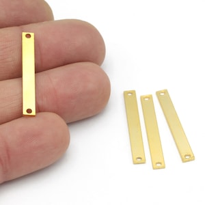 May include: Four gold-colored metal bar pendants with two holes each. The pendants are approximately 1 inch long and 1/4 inch wide.