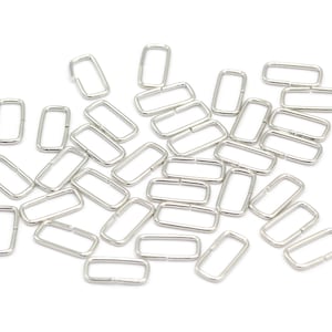 May include: A pile of silver-toned metal jump rings, also known as key rings, are scattered on a white background. These rings are commonly used for jewelry making, crafting, and attaching keys.