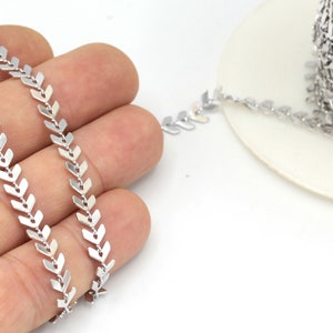 May include: Silver metal chain with a chevron pattern. The chain is made of small, pointed links that are connected to form a continuous line.