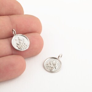 May include: Two silver charms with a raised design of a stylized flame. The charms are round and have a hole at the top for attaching to a chain or bracelet.