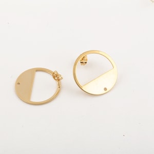 Pode incluir: Um par de brincos dourados com um design de meio círculo. Cada brinco tem um pequeno furo na parte inferior.
