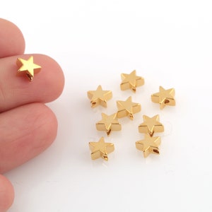 Può includere: Un gruppo di otto perline dorate a forma di stella. Le perline sono piccole e hanno una finitura lucida.