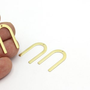 May include: Three gold metal arch-shaped charms with a small hole at the top. The charms are different sizes.