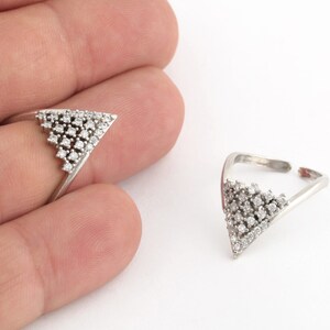 Puede incluir: Dos anillos de plata con forma de triángulo engastados con pequeñas piedras transparentes.