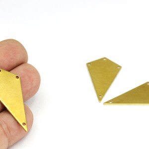 May include: Three gold-colored metal kite shapes with rounded edges and holes in the corners. The kite shapes are on a white surface.