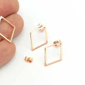 Pode incluir: Um par de brincos de diamante em forma de diamante de ouro rosa com um design simples e minimalista. Os brincos são feitos de um fio de metal fino e têm um fecho de poste.