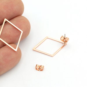 Pode incluir: Um par de brincos de diamante em forma de diamante de ouro rosa com um design simples e minimalista. Os brincos são feitos de um fio de metal fino e têm um fecho de poste.