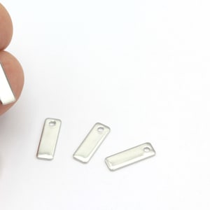May include: Four silver metal rectangular tags with a small hole at the top. The tags are flat and shiny.