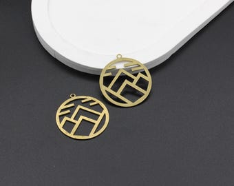 以下が含まれることがあります： 幾何学的な山のデザインが施された、金色の金属製のチャームが2つ。チャームは丸型で、上部にネックレスやブレスレットに取り付けるための穴が開いています。