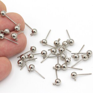 May include: A pile of silver-toned earring posts with small round balls at the top. The posts are approximately 2.5 cm long.