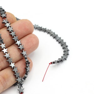 May include: A strand of grey star-shaped hematite beads. The beads are strung on a red thread.