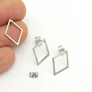 Puede incluir: Un par de pendientes de plata en forma de diamante con un diseño simple y minimalista. Los pendientes están hechos de metal y tienen un centro hueco.