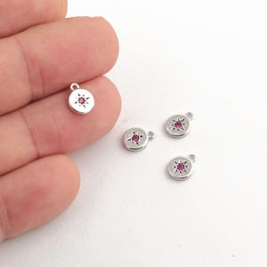 May include: Four silver charms featuring a pink star in the centre. The charms have a loop at the top for attaching to a necklace or bracelet.