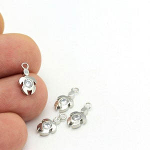 May include: Four silver turtle charms with clear rhinestone accents. The charms have a loop at the top for attaching to jewelry.