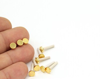 May include: A close-up of gold-toned metal discs with white ceramic posts. The discs are arranged in a row on a finger, and several more are scattered on a white surface.