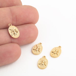 May include: Four gold-toned metal bee charms with an oval shape. Each charm features a raised bee design.