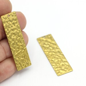 May include: Two gold-colored metal rectangular tags with a hammered texture. The tags have a hole at the top for hanging.
