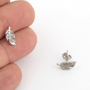 May include: A pair of silver earrings with a feather design and clear crystals.
