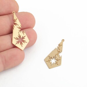 May include: Two gold-toned metal pendant charms with a starburst design. The charms are shaped like a teardrop with a pointed tip and a flat base. The starburst design is cut out of the metal, creating a delicate and intricate pattern.